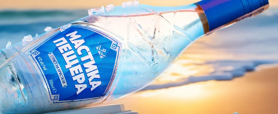 Mastika Peshtera – eisgekühlte Flasche bulgarischer Anisspirituose am sonnigen Strand mit Meereskulisse. Sommerliches Genussgetränk mit erfrischendem Geschmack und Eiskristallen.